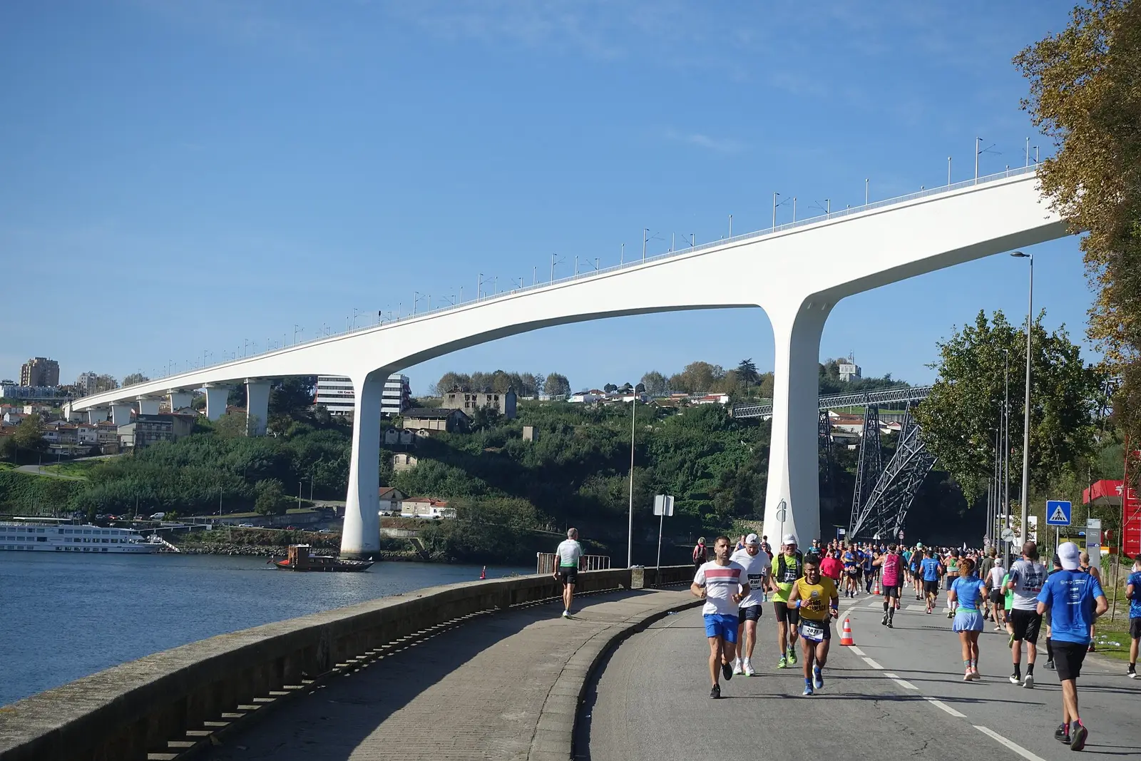 Marathon runners on the Douro riverside road below a white bridge in Porto